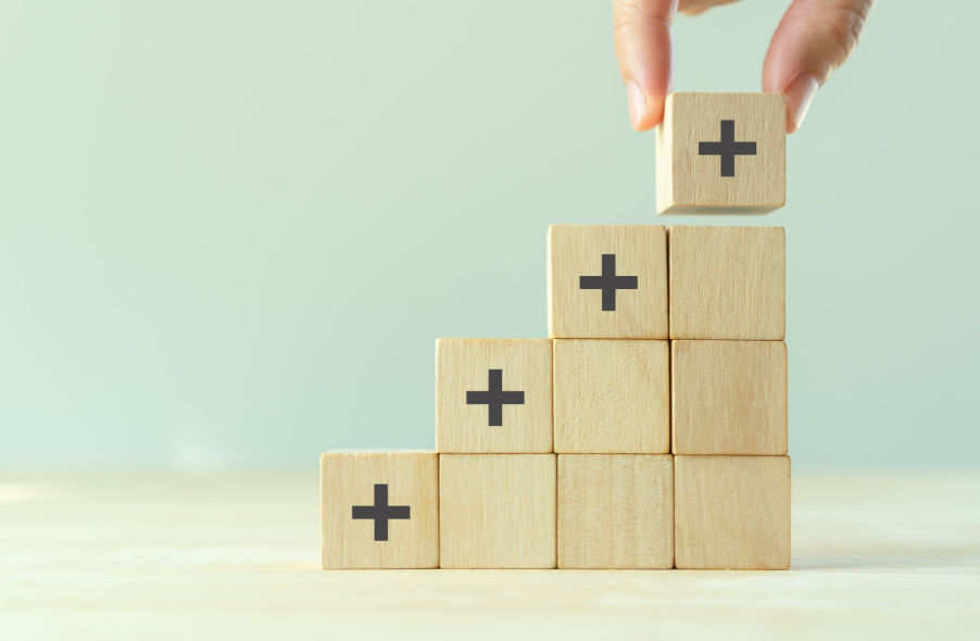 hand stacking wooden cube with plus sign